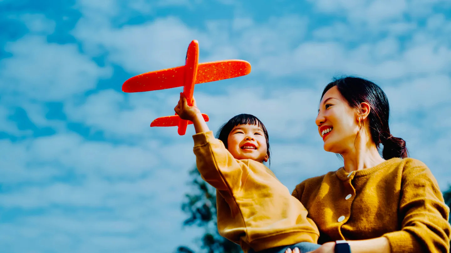 A toddler playing with a toy airplane in her mum's arms.