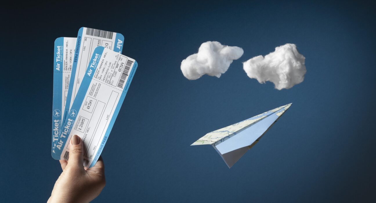 A hand holding boarding passes with A paper Airplane and Cotton made clouds in the background.