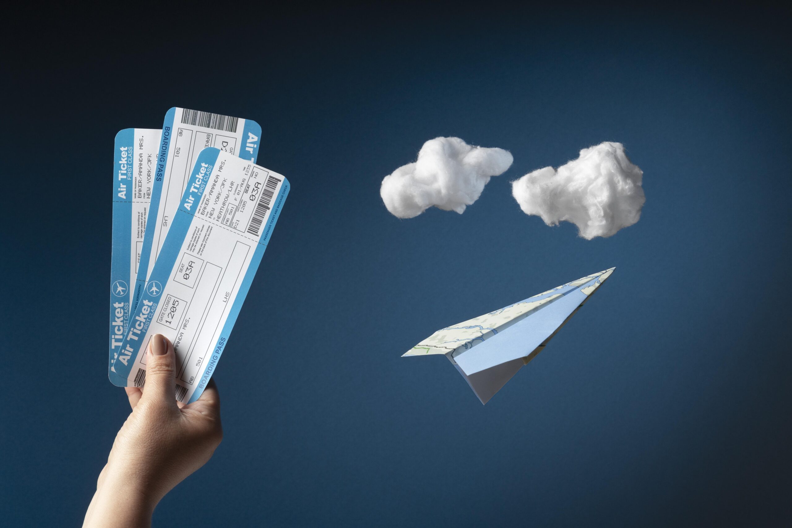 A hand holding boarding passes with A paper Airplane and Cotton made clouds in the background.