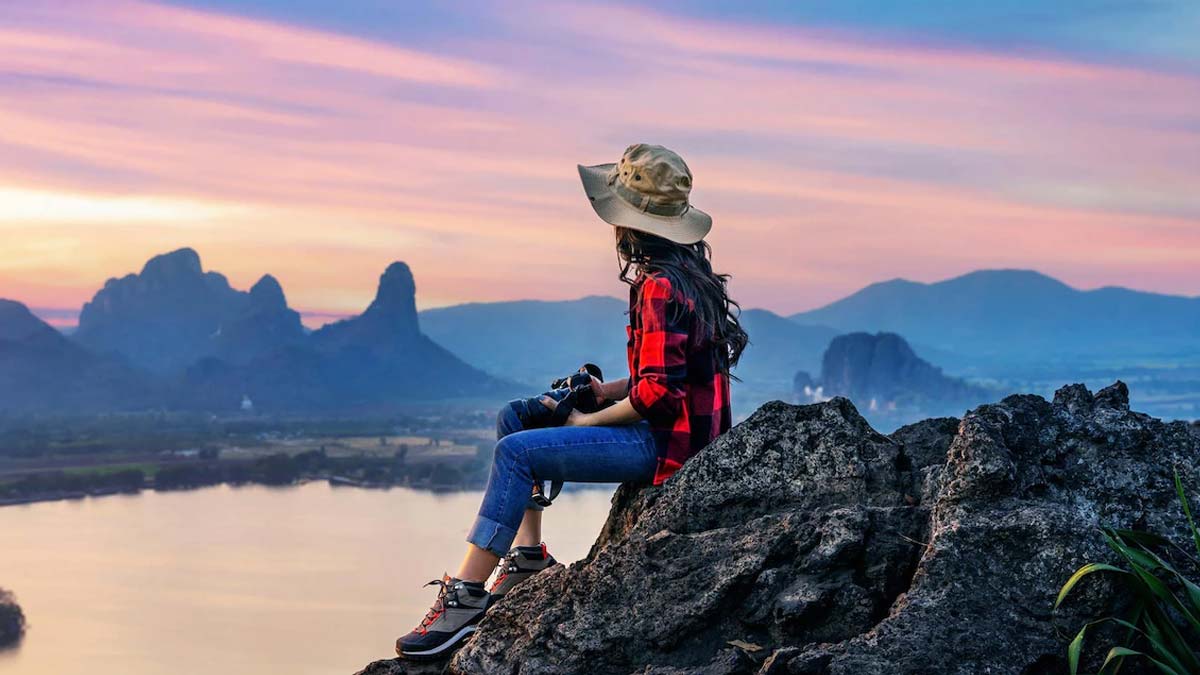 A female solo traveler sitting on a mountain peak.